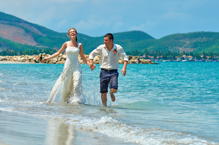 Bride and groom running along the beach